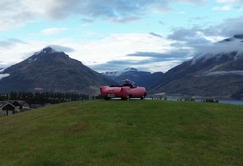 The little pink car parked above the lake with mountains beyond